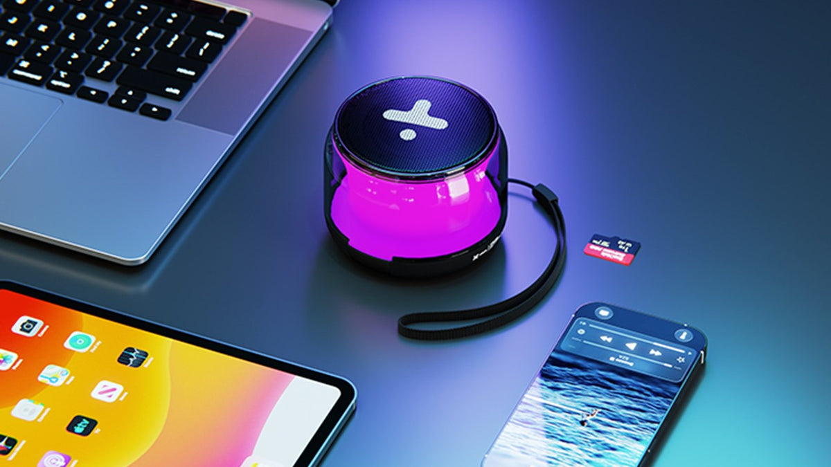 Bocina Xtech Halen con luces LED rosadas y correa junto a una computadora, tableta y teléfono