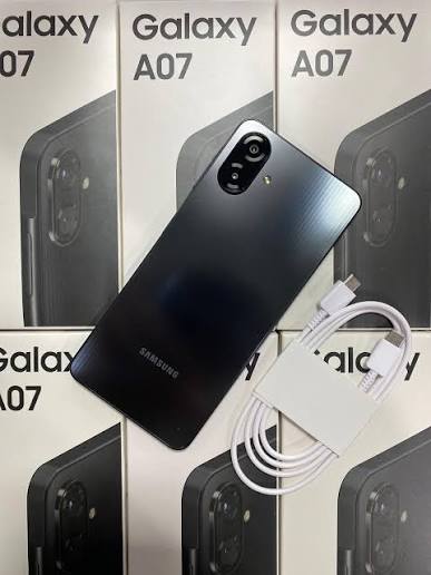 Samsung Galaxy A07 oscuro junto a cable y cargador sobre cajas del modelo