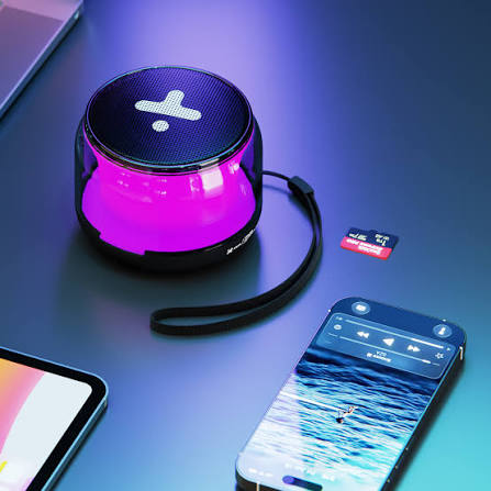 Bocina portátil Xtech Halen iluminada en color rosado junto a un teléfono